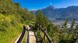 Hotels Marling: alpin-mediterrane Idylle Wanderweg mit Holzzaun und Stadtblick vor Berglandschaft unter klarem Himmel