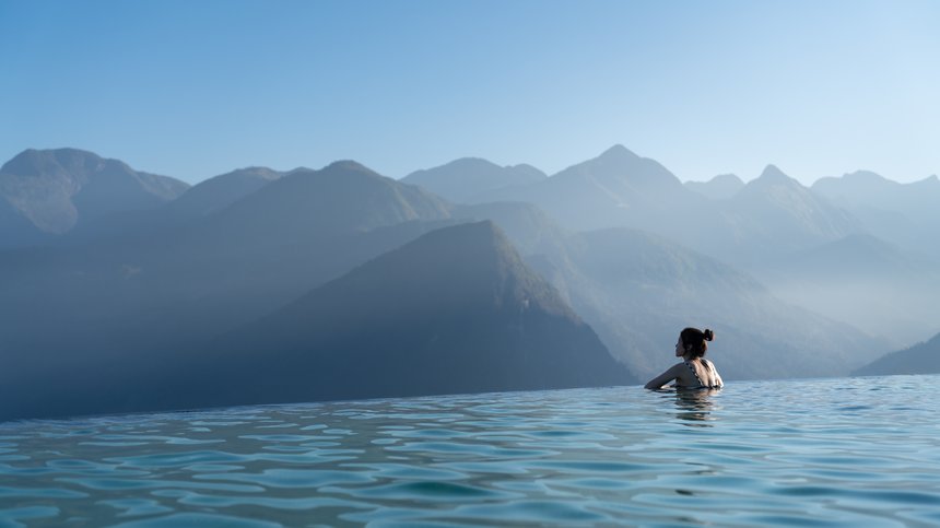 Hotel in Alto Adige 😎☀️ Per vacanze indimenticabili Donna in piscina a sfioro che guarda montagna nebbiosa sotto cielo limpido