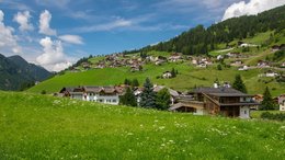 Hotel sulle Dolomiti Prati verdi con case ai piedi di colline boschive sotto un cielo blu