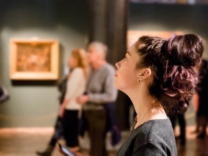 Hotel a Plan de Corones Donna che guarda una mostra al museo con altri visitatori sfocati sullo sfondo