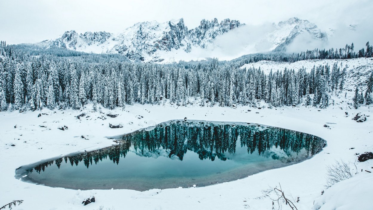 Schneeschuhwandern in Welschnofen Schneebedeckter Bergsee mit reflektierenden Tannen und Nebel