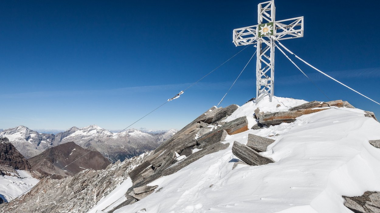 Punta Bianca nelle Valli di Tures e Aurina Croce metallica su cima innevata con vista sulle montagne sotto un cielo blu