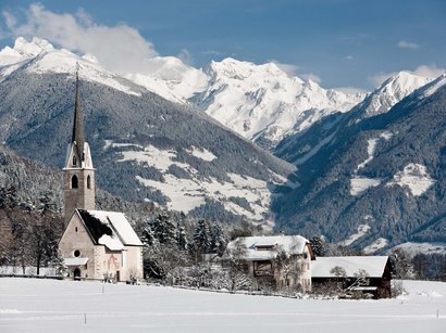 Sonnenloipe Kasern Schneebedeckte Kirche und Häuser vor Berglandschaft im Winter