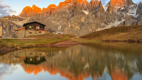 Sul Passo Rolle Rifugio alpino con montagne illuminate dal tramonto e riflesso nel lago