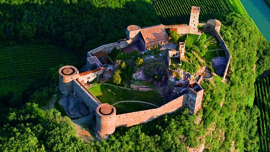 Castel Firmiano: fortezza romanica con museo Veduta aerea di un castello su una collina boschiva con vigneti e fiume