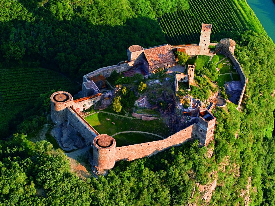 Schloss Sigmundskron: romanische Festung mit Museum Luftaufnahme einer Burg auf einem bewaldeten Hügel mit Weinbergen und Fluss