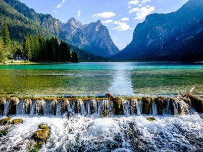 Die schönsten Seen in Südtirol Klares Bergseenwasser mit kleinem Wasserfall und bewaldeten Bergen im Hintergrund