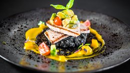 ABINEA Dolomiti Romantic SPA Hotel Gourmetgericht mit gegrilltem Fisch, Avocado und Gemüse auf schwarzem Teller