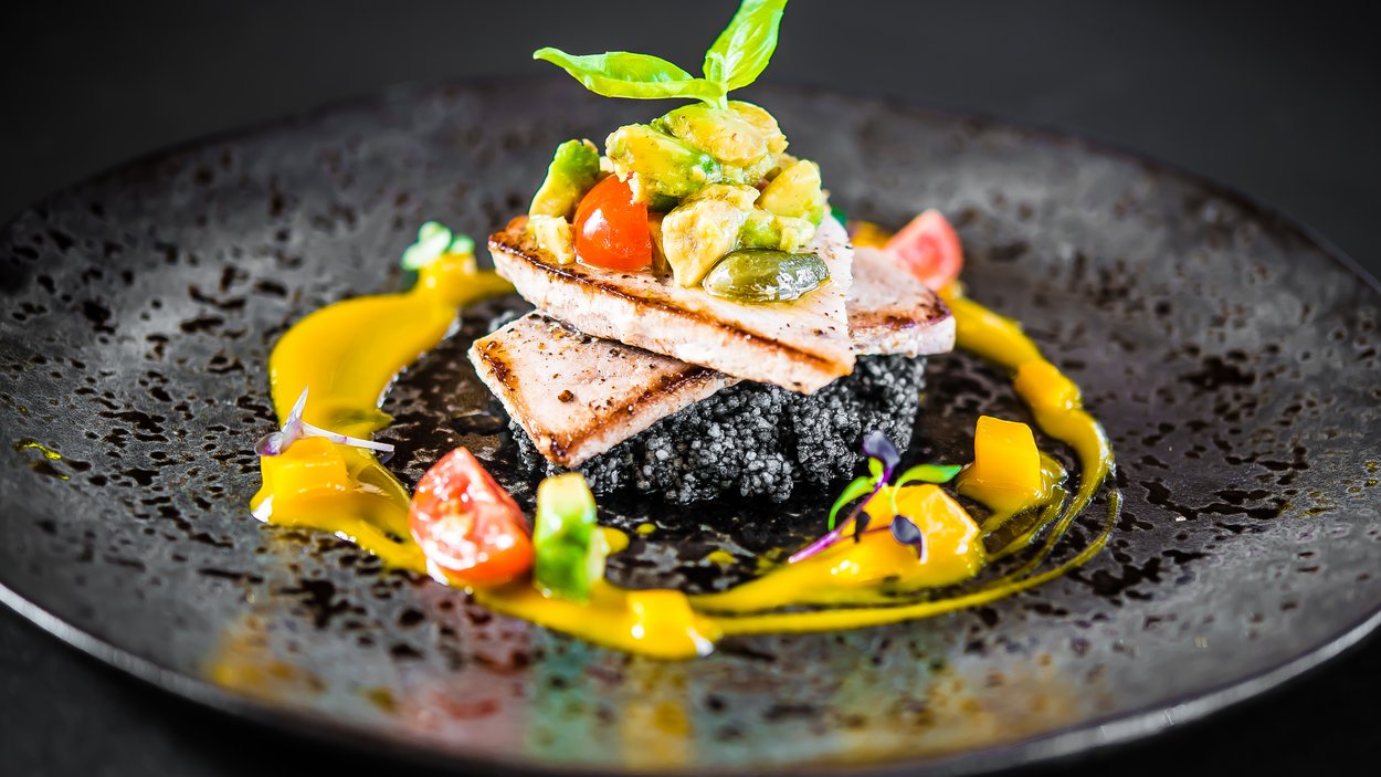 Gourmet-Urlaub in Südtirol: Genuss pur Gourmetgericht mit gegrilltem Fisch, Avocado und Gemüse auf schwarzem Teller