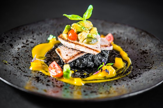 Gourmet-Urlaub in Südtirol: Genuss pur Gourmetgericht mit gegrilltem Fisch, Avocado und Gemüse auf schwarzem Teller