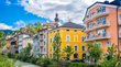 Il vostro hotel a Brunico! Case colorate lungo un fiume in una città sotto un cielo nuvoloso