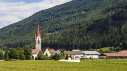 Hotel a Racines presso Vipiteno Villaggio con torre della chiesa davanti a montagna boscosa e campi verdi