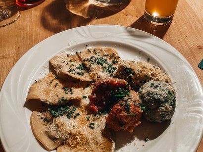 Törggelen in Südtirol: Topangebote mit Übernachtung Teller mit verschiedenen gefüllten Teigtaschen und Getränken auf Holztisch