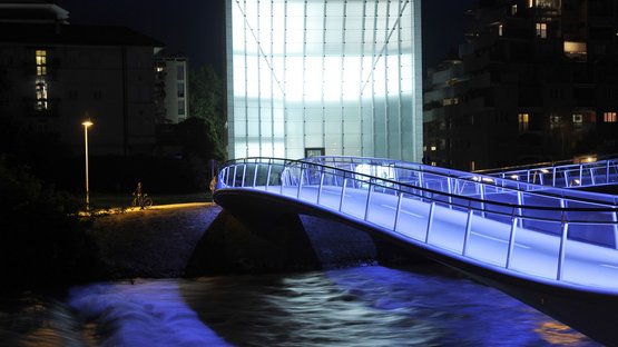 Das Museion in Bozen Beleuchtete moderne Brücke über einen Fluss bei Nacht mit blauem Licht