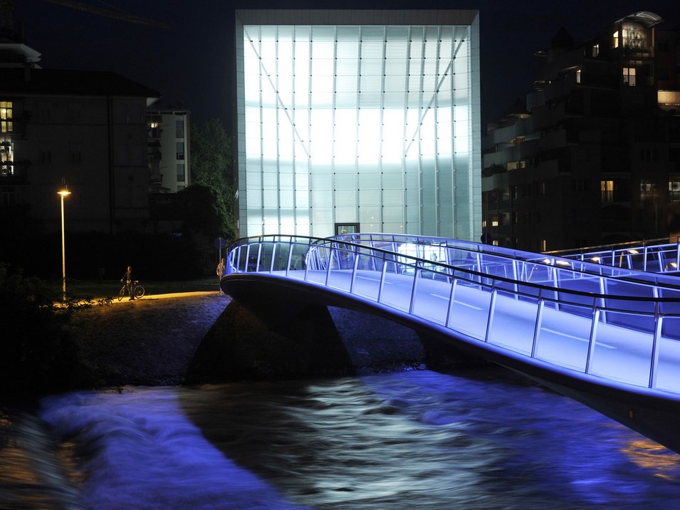 Das Museion in Bozen Beleuchtete moderne Brücke über einen Fluss bei Nacht mit blauem Licht
