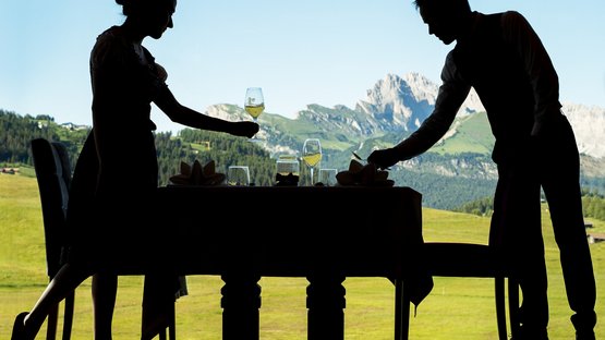 Gourmet-Urlaub in Südtirol: Genuss pur Silhouetten von Kellnern beim Decken eines Tisches mit Bergblick