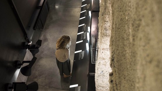 Das Benediktinerstift Marienberg Frau betrachtet beleuchtetes Ausstellungspanel neben einer alten Steinwand im Museum