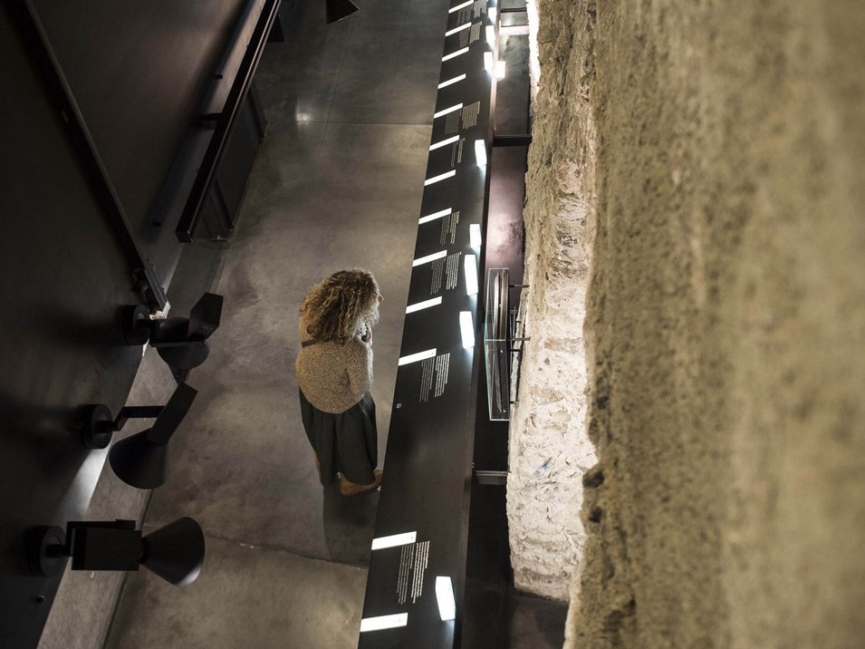 Das Benediktinerstift Marienberg Frau betrachtet beleuchtetes Ausstellungspanel neben einer alten Steinwand im Museum