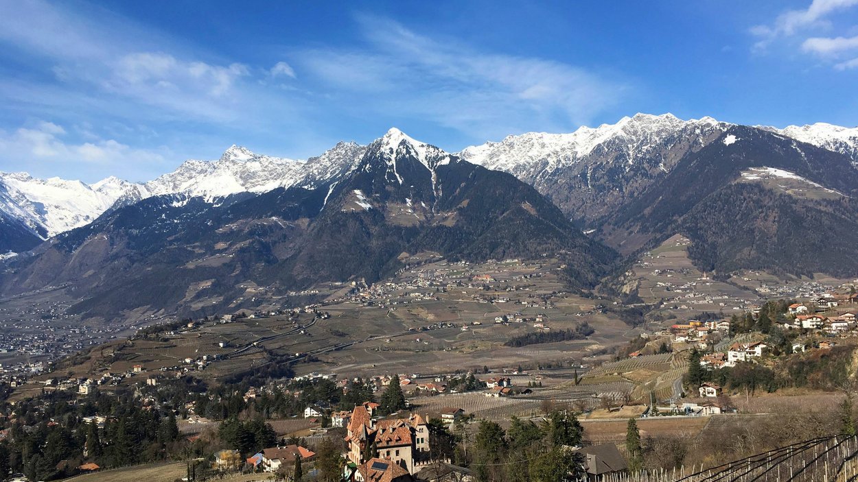 Hotels in Dorf Tirol: Ihre Lieblingsdestination Landschaft mit schneebedeckten Bergen und Weinbergen unter blauem Himmel