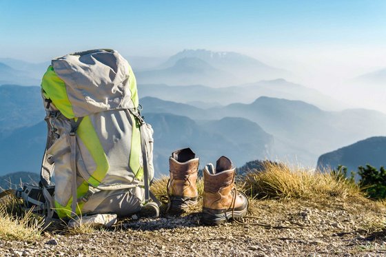 Trentino-Südtirol entdecken Rucksack und Wanderschuhe auf Berggipfel mit nebligen Bergen im Hintergrund