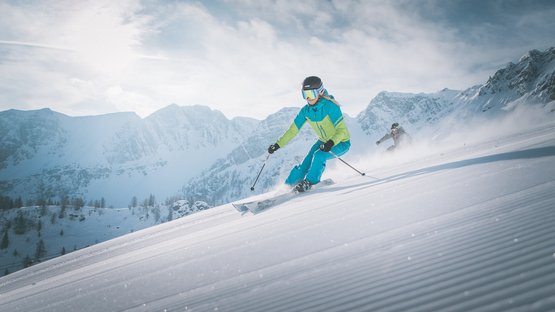 Das Familienparadies für Ihren Winterurlaub Zwei Skifahrer fahren einen schneebedeckten Hang in den Bergen hinunter