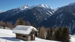 Ihre Hotels in Meran in Südtirol: Hotels im Meraner Land Kleine verschneite Holzhütte vor schneebedeckten Bergen und Nadelbäumen