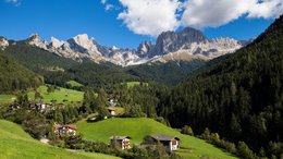 Hotels auf der Seiser Alm: unter Alpengipfeln genießen Bergdorf mit grünen Wiesen und Nadelwald vor Felsformationen bei klarem Himmel