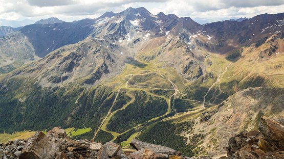 Hochalpine Tour im Vinschgau Blick auf felsige Alpenberge mit grünen Tälern und Wanderwegen unter bewölktem Himmel