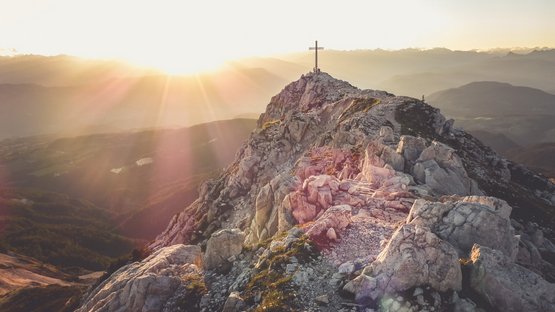 Vie ferrate in Alto Adige Vettta di montagna rocciosa con croce e sentiero al sorgere del sole