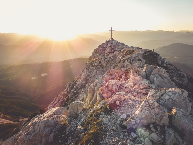 Vie ferrate in Alto Adige Vettta di montagna rocciosa con croce e sentiero al sorgere del sole