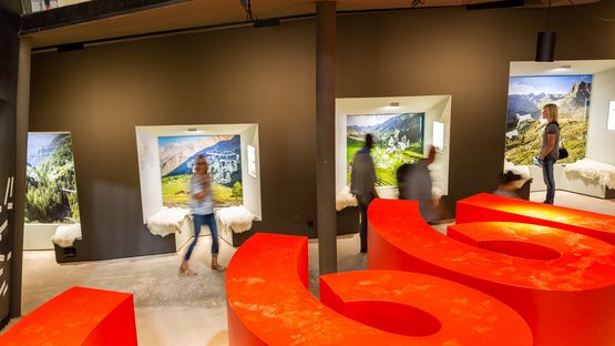 Un curioso memoriale in Alto Adige Interno con sedute rosse e persone davanti a fotografie di montagne