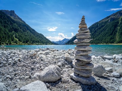 Die schönsten Seen in Südtirol Aufgestapelte Steine am Ufer eines Bergsees mit Bergen im Hintergrund