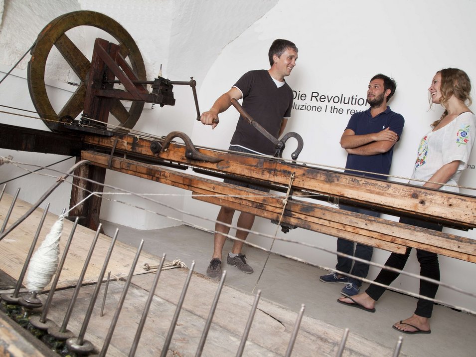Il museo Uomo nel tempo a Cortaccia Tre persone utilizzano un antico telaio in mostra museale