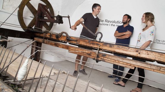 Das Museum Zeitreise Mensch in Kurtatsch Drei Menschen bedienen historische Webmaschine in Museumsausstellung