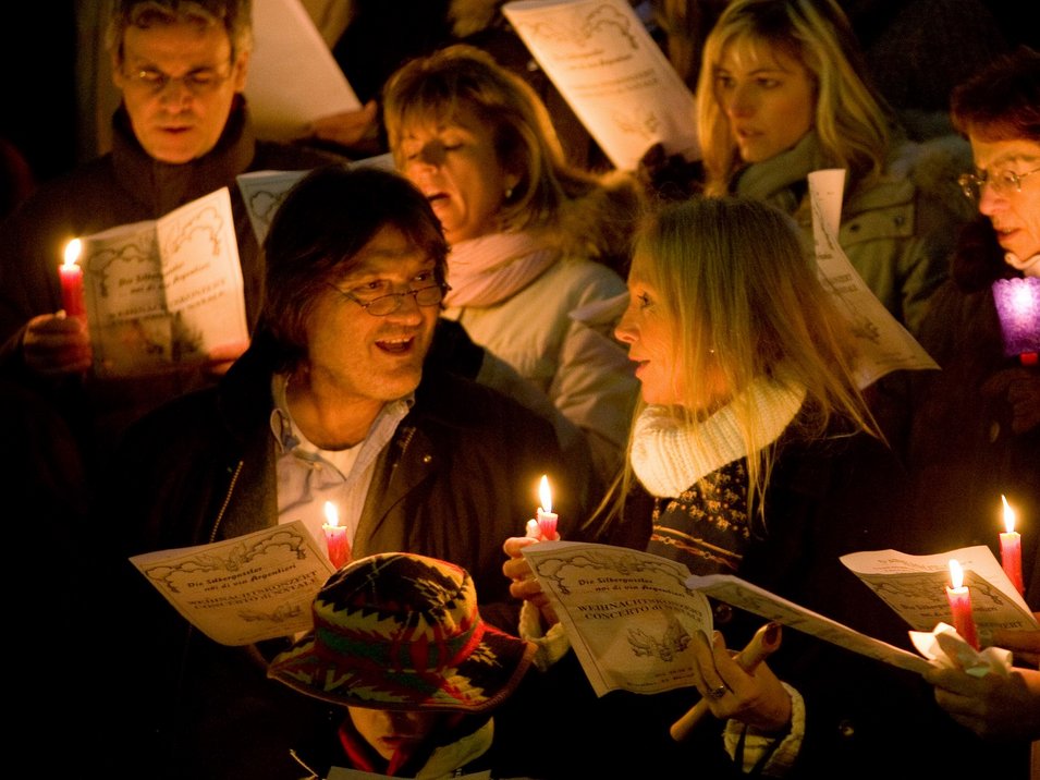 Mercatino di Natale di Castel Tirolo Persone che cantano a lume di candela tenendo fogli di canzoni
