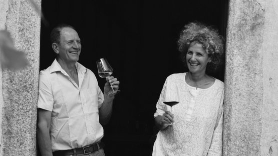 Tenuta Kränzelhof – un’esperienza che risveglia i sensi Due persone sorridenti scalze in un telaio di porta con calici di vino