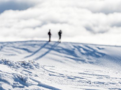 Winterwanderung Haidenberg Zwei Personen stehen auf einem schneebedeckten Hügel unter bewölktem Himmel
