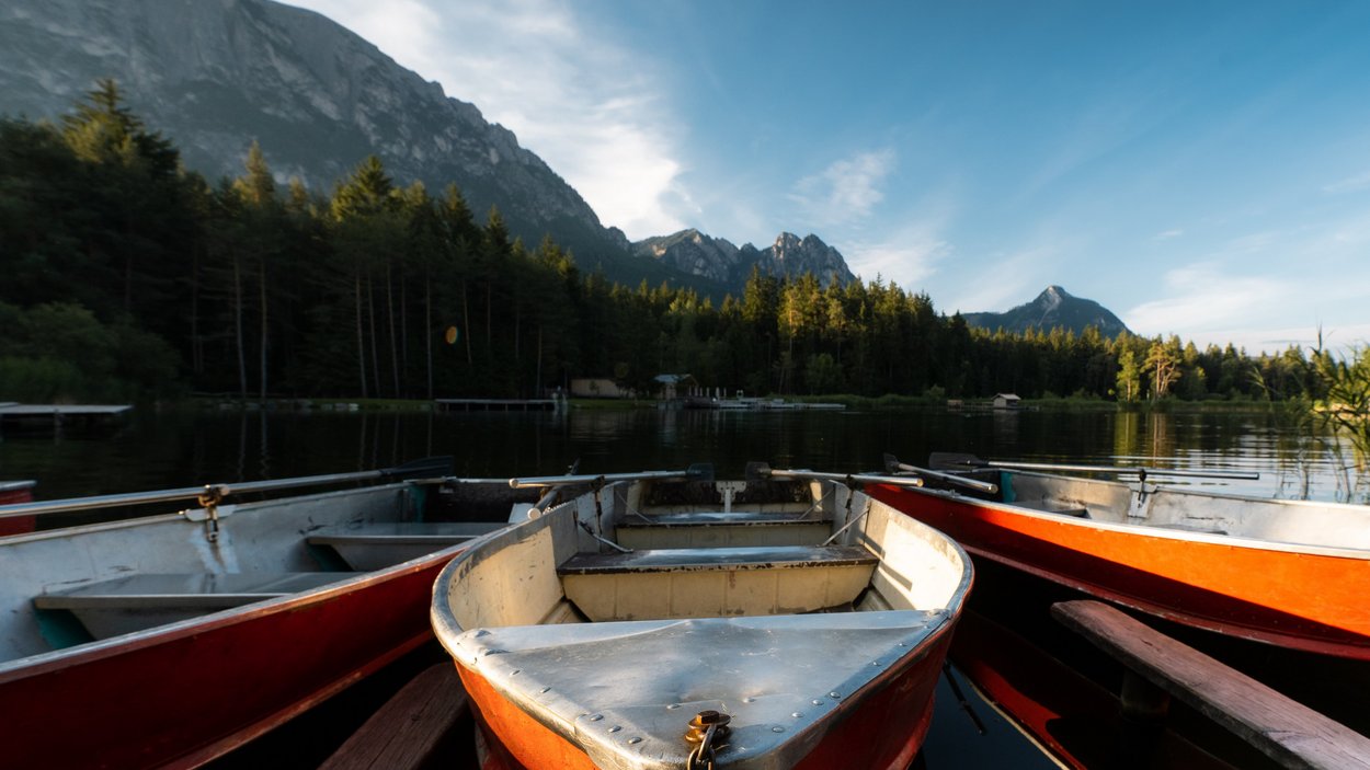 Die schönsten Seen in Südtirol Drei Ruderboote auf einem See vor bewaldeten Bergen bei sonnigem Himmel