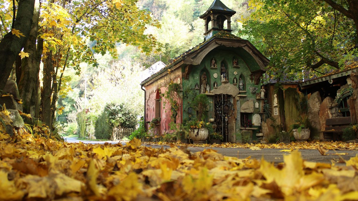 K. u. K. Museum Bad Egart Kleine bunte Kapelle umgeben von Herbstlaub und Bäumen an einem Landweg