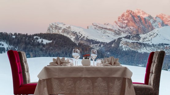 Hotel gourmet in Alto Adige Tavolo elegante apparecchiato davanti a grande finestra con vista su montagne innevate