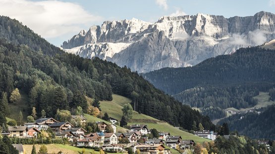 Hotels in St. Ulrich in Gröden – Südtirol-Urlaub vom Feinsten Dorf mit Häusern vor bewaldeten Hügeln und Felsgebirge im Hintergrund