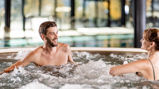 Cercasi hotel a 4 stelle in Alto Adige? Eccoli qui! Uomo e donna si rilassano in una vasca idromassaggio con acqua frizzante al chiuso