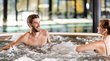 Cercasi hotel a 4 stelle in Alto Adige? Eccoli qui! Uomo e donna si rilassano in una vasca idromassaggio con acqua frizzante al chiuso