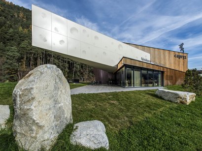 La miniera di Villandro, un pezzo di storia Edificio moderno con facciata in legno e grandi pietre su prato verde