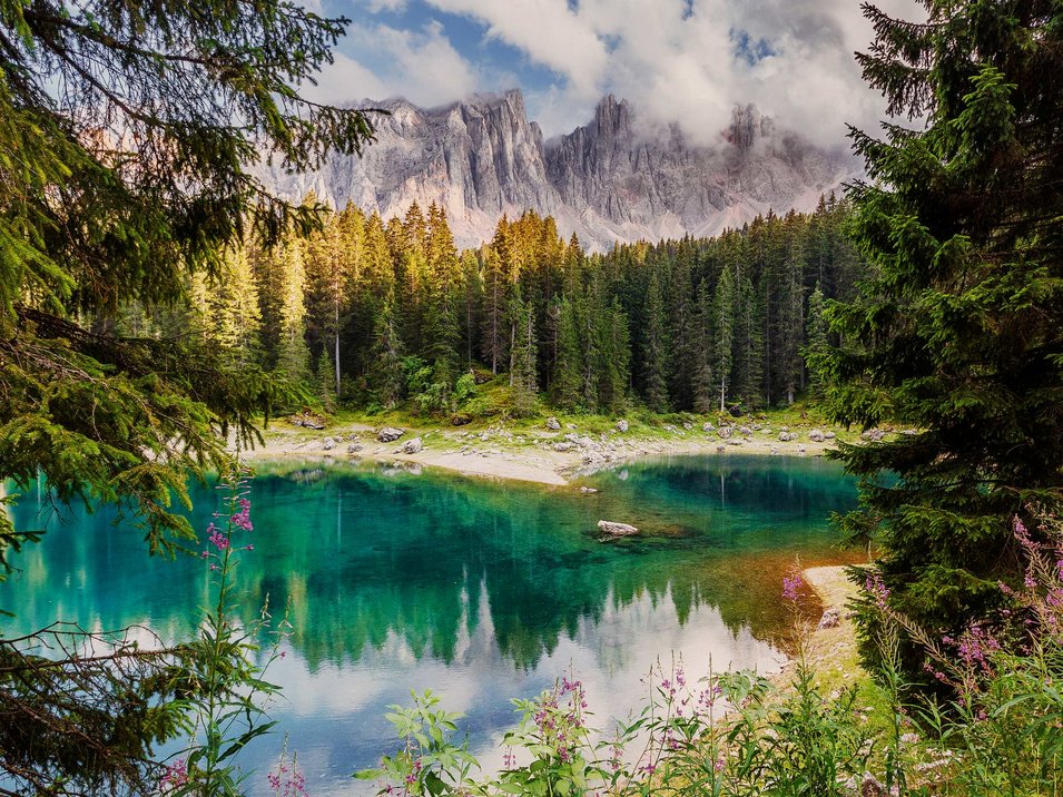 Hotels am Rosengarten und Latemar Klare Berglandschaft mit blauem See, grünen Bäumen und bewölktem Himmel
