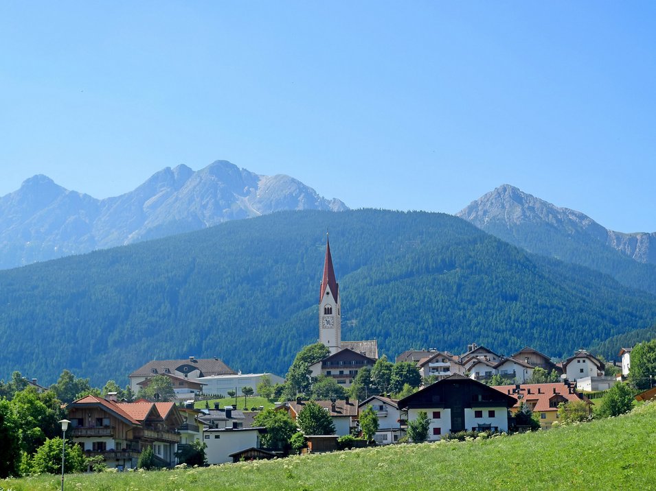 Hotel a Valdaora in Alta Pusteria Villaggio con chiesa davanti a montagne verdi e cielo azzurro