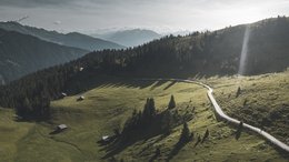 Hotels Eisacktal, Südtirol: Hotels in Brixen, Klausen … Berglandschaft mit grasbewachsenen Hügeln, Wald und kurviger Straße bei Sonnenlicht