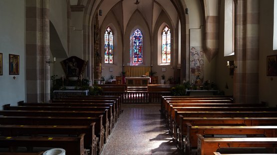 Hotels in Glurns: Urlaub in der kleinsten Stadt Südtirols Innenraum einer Kirche mit Holzbänken und bunten Buntglasfenstern am Altar
