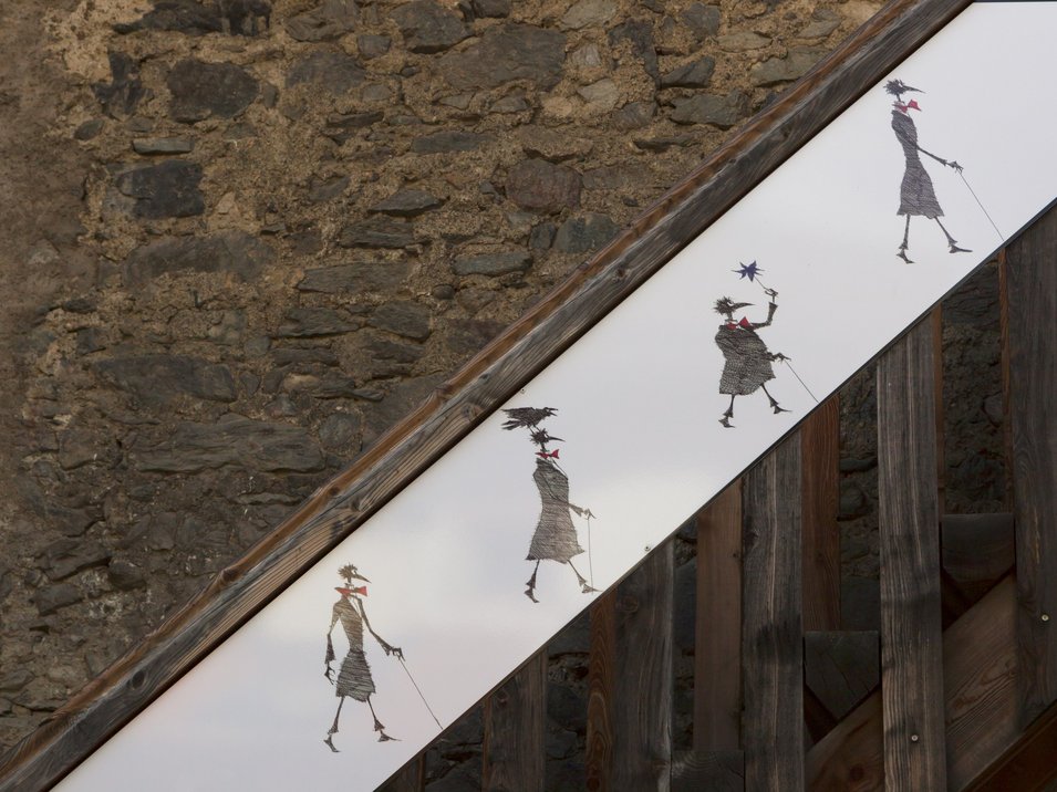 Kirchtorturm Paul Flora in Glurns Wandkunst auf Treppe zeigt vier schemenhafte Figuren mit Regenstielen und Schirmen