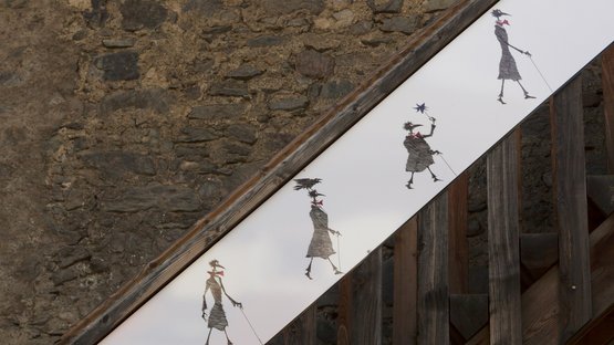 Kirchtorturm Paul Flora in Glurns Wandkunst auf Treppe zeigt vier schemenhafte Figuren mit Regenstielen und Schirmen
